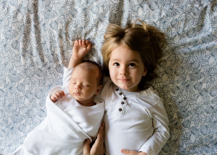Una niña junto a un bebé en una cama